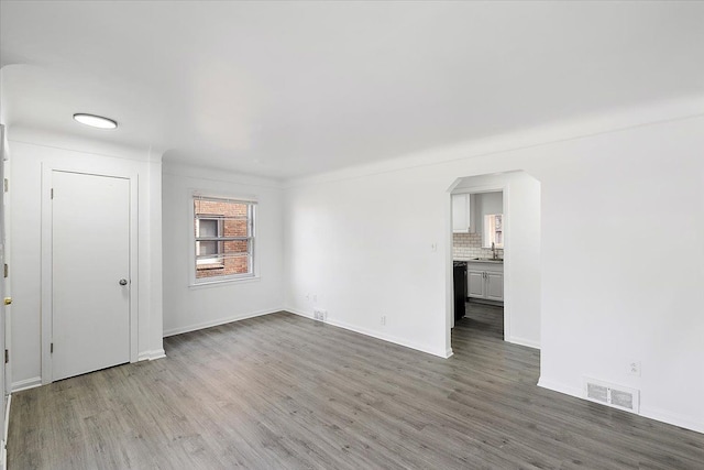 empty room featuring arched walkways, visible vents, a sink, and wood finished floors