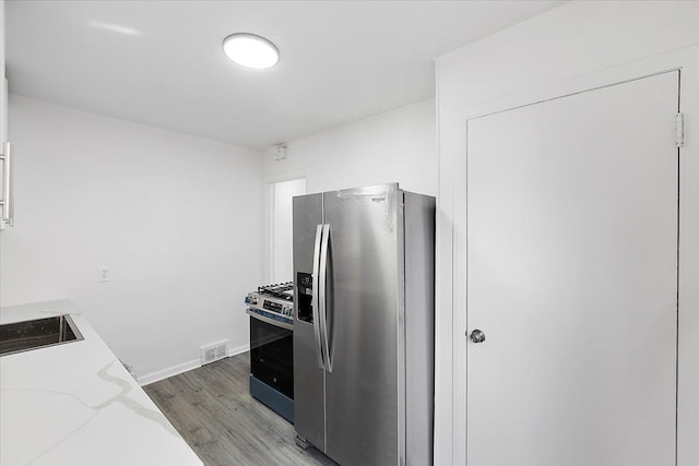 kitchen featuring light wood finished floors, visible vents, light stone counters, stainless steel appliances, and a sink