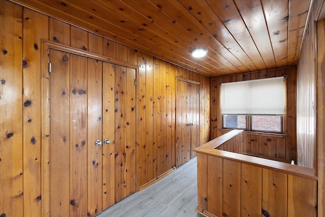 hallway featuring wooden walls, an upstairs landing, wood ceiling, and light wood-type flooring