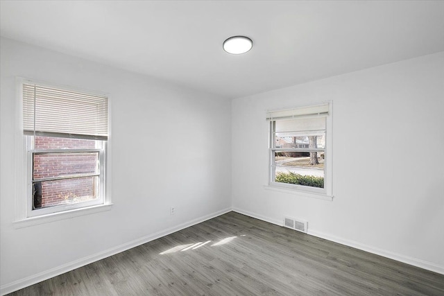 empty room featuring wood finished floors, visible vents, and baseboards