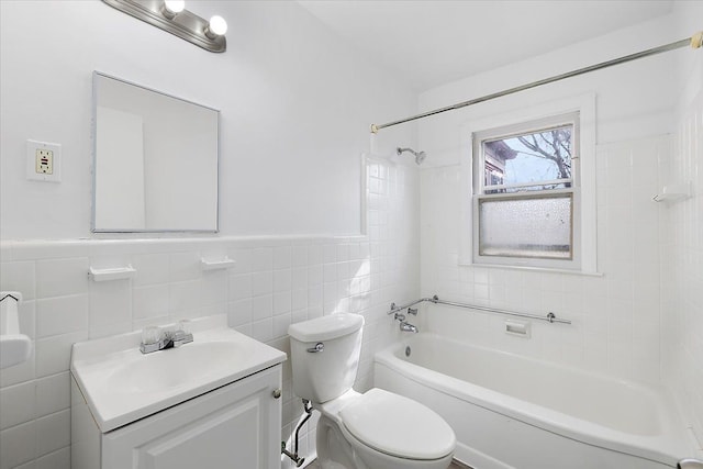 bathroom featuring shower / washtub combination, toilet, vanity, wainscoting, and tile walls