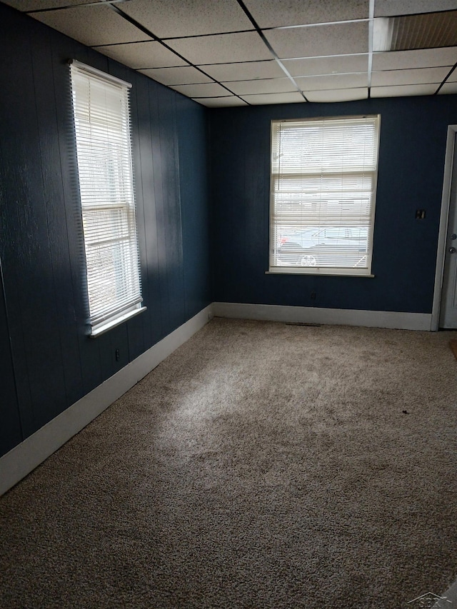 carpeted empty room with wooden walls, a paneled ceiling, and baseboards