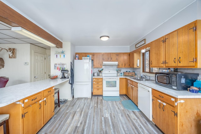 kitchen with under cabinet range hood, a sink, backsplash, white appliances, and a peninsula