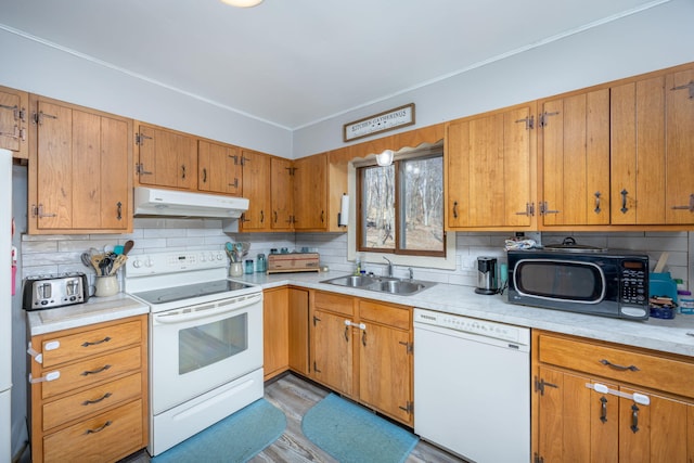 kitchen featuring under cabinet range hood, light countertops, brown cabinetry, white appliances, and a sink