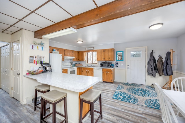 kitchen featuring white appliances, a peninsula, light countertops, light wood-style floors, and under cabinet range hood