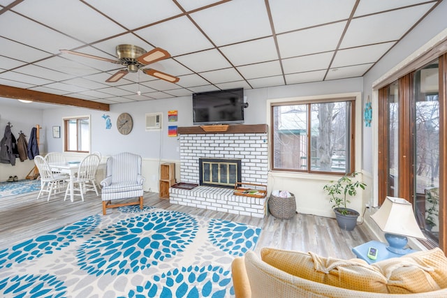 living room with a brick fireplace, wood finished floors, a drop ceiling, and ceiling fan