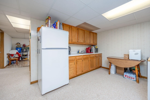 kitchen with wallpapered walls, a drop ceiling, freestanding refrigerator, a sink, and light countertops