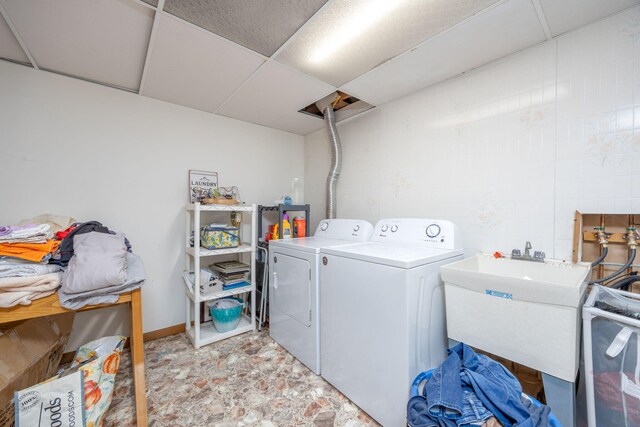 clothes washing area with stone finish floor, a sink, separate washer and dryer, baseboards, and laundry area