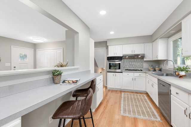 kitchen with built in study area, a sink, stainless steel appliances, under cabinet range hood, and a kitchen breakfast bar