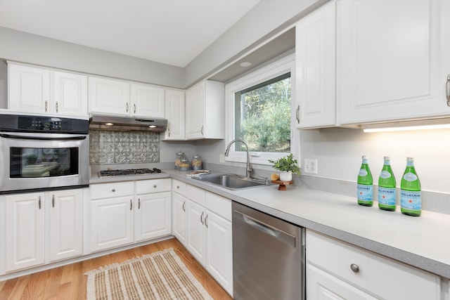 kitchen with light wood-style flooring, a sink, stainless steel appliances, light countertops, and under cabinet range hood