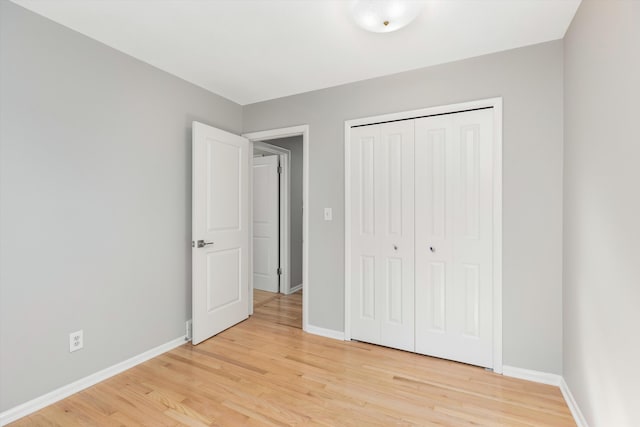 unfurnished bedroom featuring light wood-style flooring, baseboards, and a closet