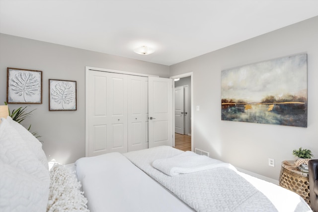 bedroom with wood finished floors, visible vents, and a closet