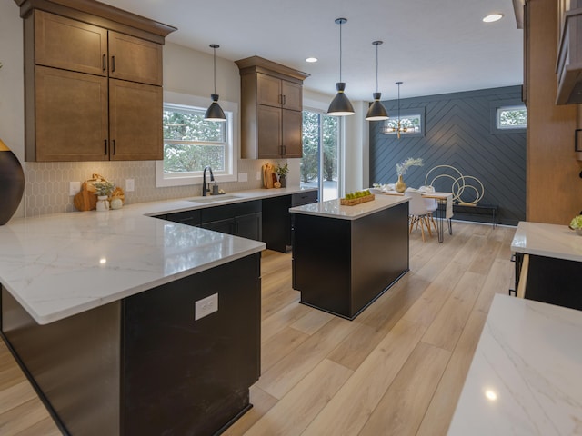 kitchen featuring tasteful backsplash, light stone counters, a peninsula, light wood-style floors, and a sink