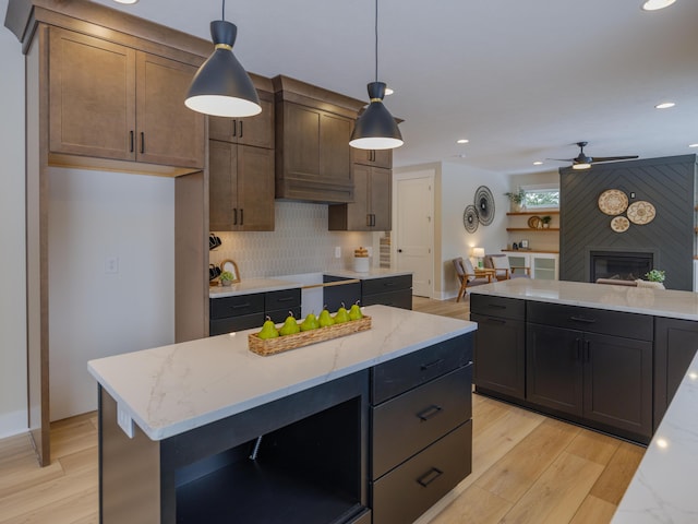 kitchen with light wood-style flooring, backsplash, a fireplace, light stone countertops, and hanging light fixtures