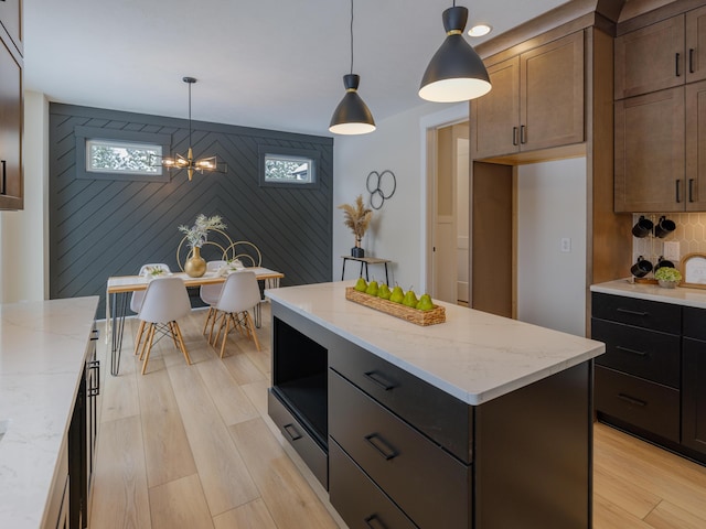 kitchen featuring light stone counters, decorative light fixtures, a kitchen island, and light wood-style flooring