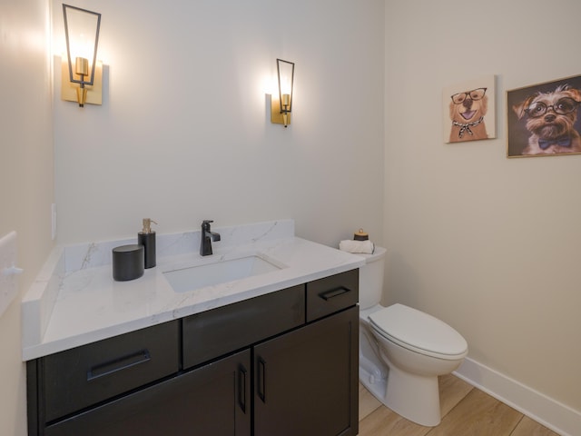 half bath with baseboards, toilet, wood finished floors, and vanity