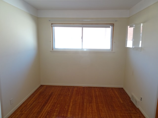 empty room featuring wood finished floors, visible vents, and baseboards