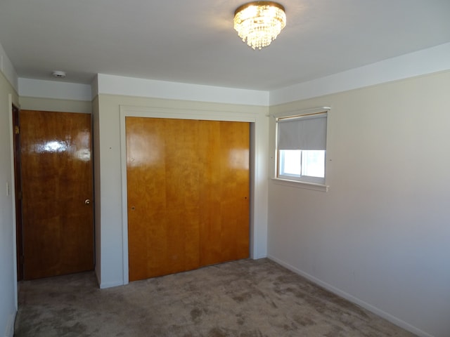 unfurnished bedroom with a closet, a notable chandelier, and carpet flooring