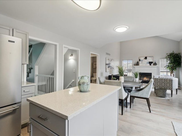 kitchen featuring a lit fireplace, gray cabinetry, freestanding refrigerator, and lofted ceiling