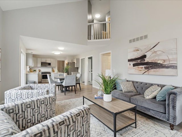 living room featuring light wood-style flooring, visible vents, and a towering ceiling