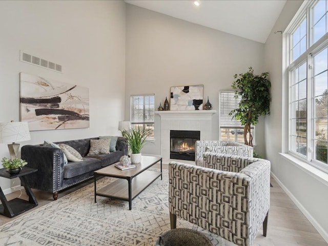 living area with visible vents, baseboards, high vaulted ceiling, and wood finished floors