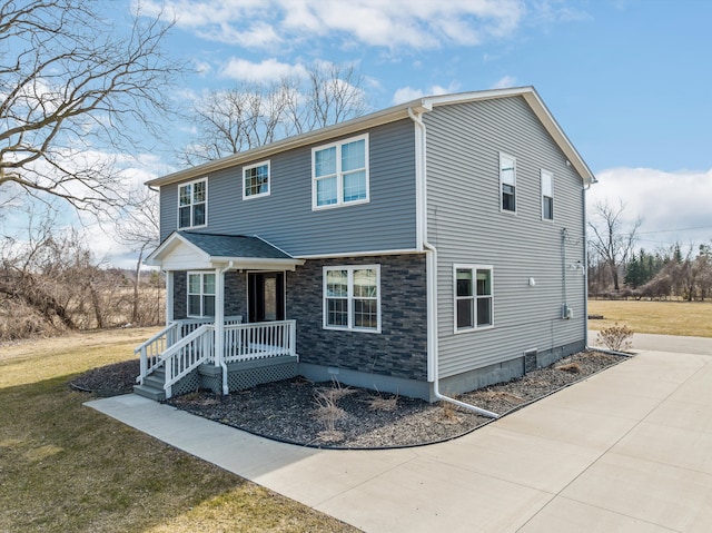 view of front of house featuring stone siding, covered porch, and a front yard