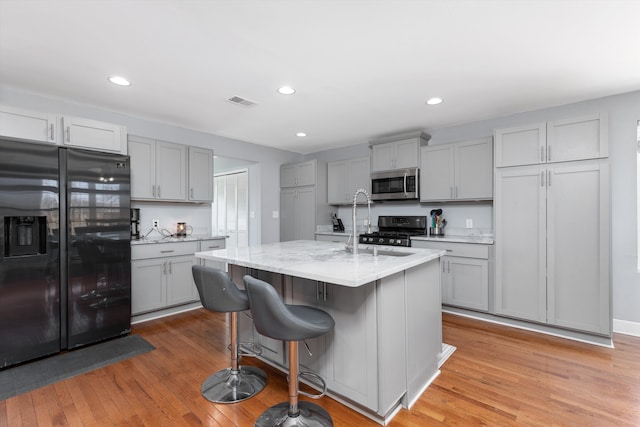 kitchen featuring stainless steel microwave, black fridge, gray cabinets, and gas range oven