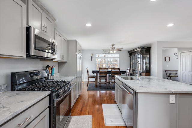 kitchen with a center island with sink, gray cabinets, a sink, appliances with stainless steel finishes, and light wood finished floors