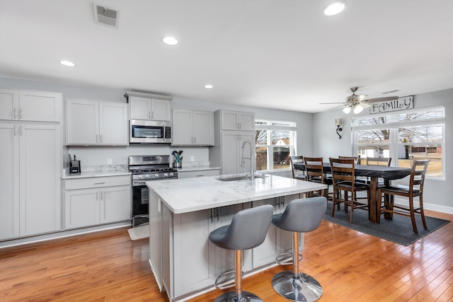 kitchen featuring visible vents, an island with sink, light wood-style flooring, stainless steel appliances, and a sink