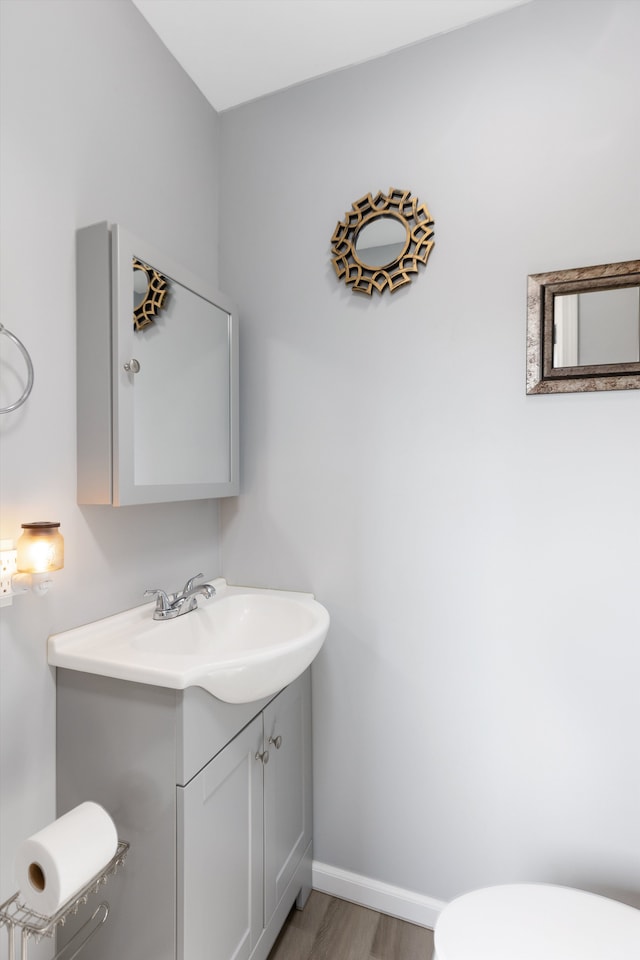 half bath featuring vanity, toilet, wood finished floors, and baseboards