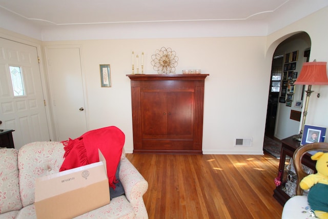 living room with arched walkways, visible vents, baseboards, and wood finished floors