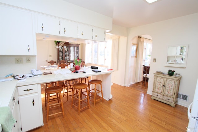 kitchen with visible vents, light wood finished floors, arched walkways, light countertops, and a kitchen bar