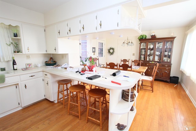 kitchen with light wood-style flooring, a peninsula, light countertops, and a kitchen breakfast bar