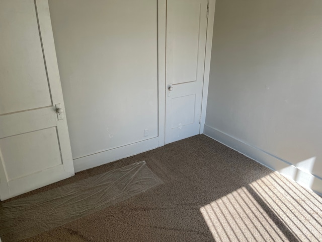 unfurnished room with baseboards and dark carpet