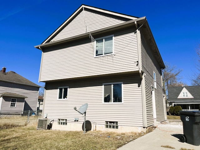 rear view of house featuring a lawn, central AC unit, and fence