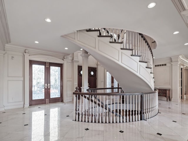 foyer entrance featuring marble finish floor, french doors, crown molding, a decorative wall, and ornate columns