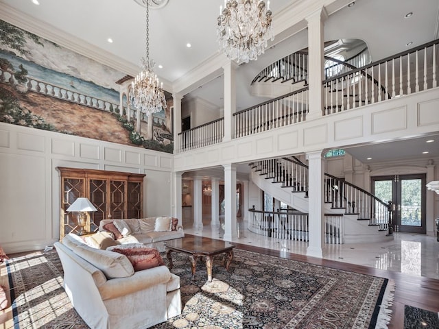 living room featuring ornamental molding, an inviting chandelier, a decorative wall, decorative columns, and stairs
