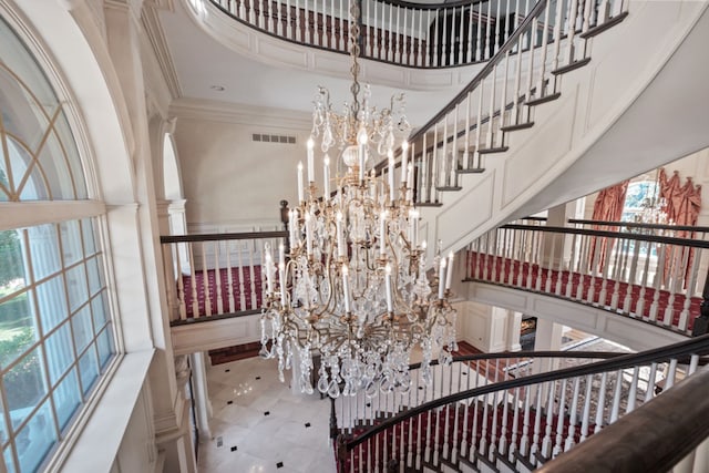 stairs with an inviting chandelier, a high ceiling, crown molding, and visible vents