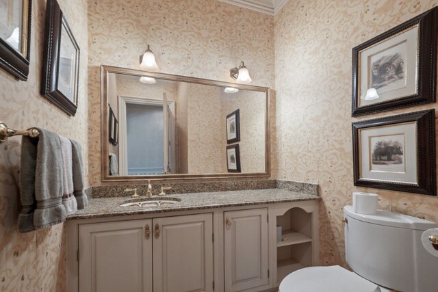 bathroom with toilet, wallpapered walls, vanity, and ornamental molding