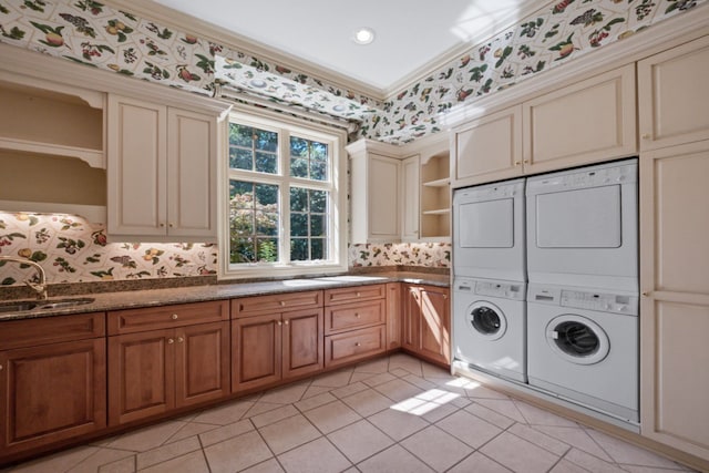 laundry room with a sink, cabinet space, crown molding, wallpapered walls, and stacked washer / dryer