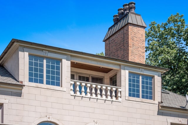 view of side of home featuring a balcony, roof with shingles, and a chimney