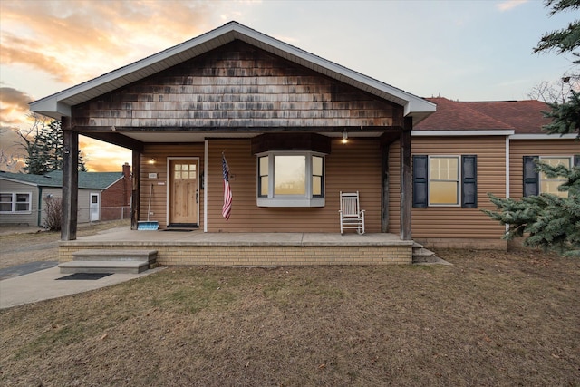 view of front of house featuring a yard, roof with shingles, and a porch