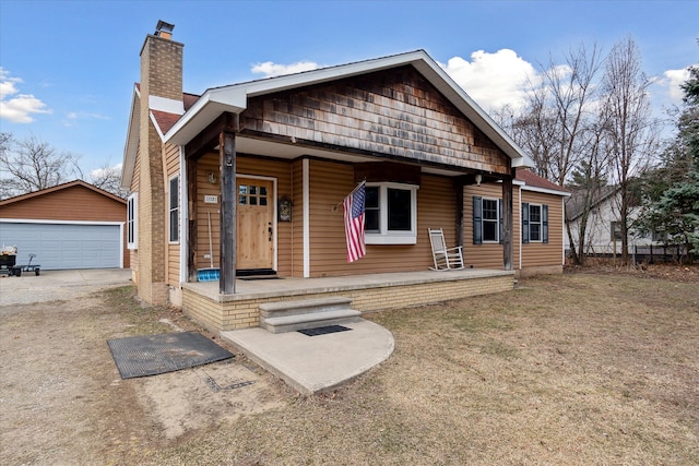 view of front of property featuring a detached garage, an outbuilding, a porch, and a chimney