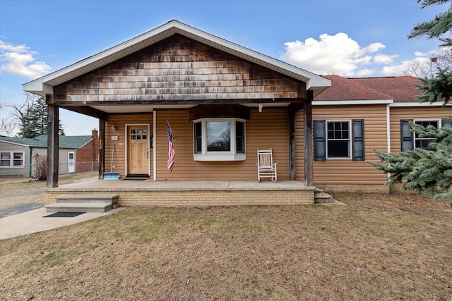 view of front of property with roof with shingles, a porch, and a front yard