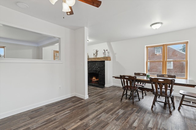 dining room featuring ceiling fan, baseboards, a stone fireplace, and dark wood finished floors