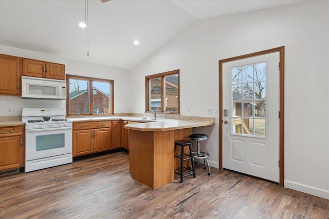 kitchen with dark wood finished floors, white appliances, lofted ceiling, and a kitchen breakfast bar