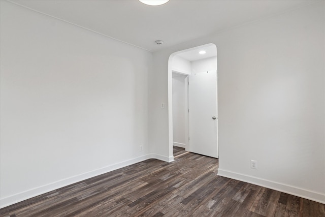 unfurnished room with baseboards, arched walkways, and dark wood finished floors