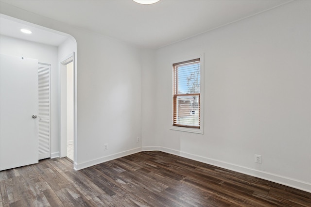 unfurnished room featuring dark wood finished floors, arched walkways, and baseboards