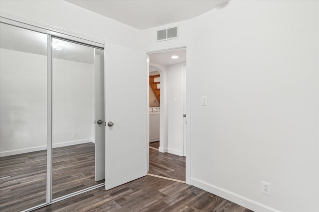 unfurnished bedroom with wood finished floors, visible vents, baseboards, arched walkways, and a closet