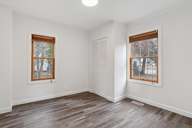 unfurnished bedroom with dark wood-type flooring, baseboards, visible vents, and a closet